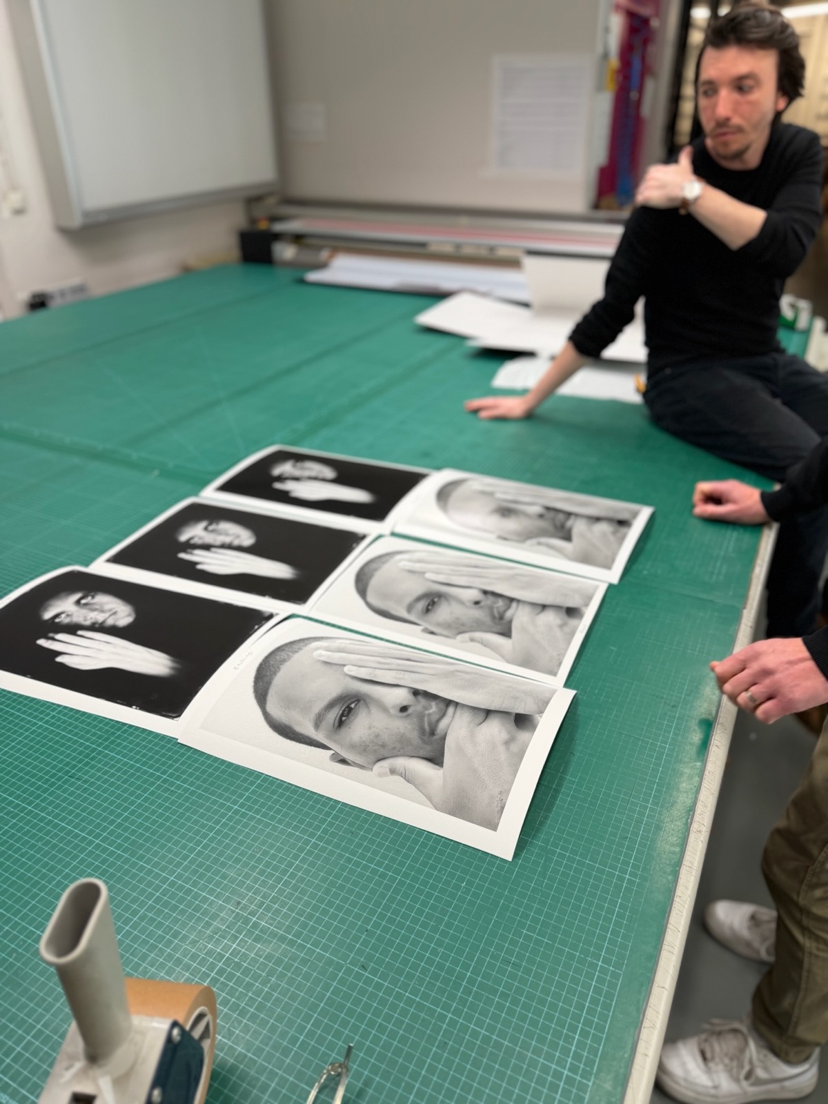 Two stacks of prints on a printmaker's table — one on black paper, one on warm white.